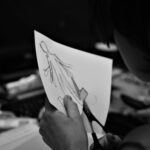 grayscale photo of woman holding pen writing on white paper