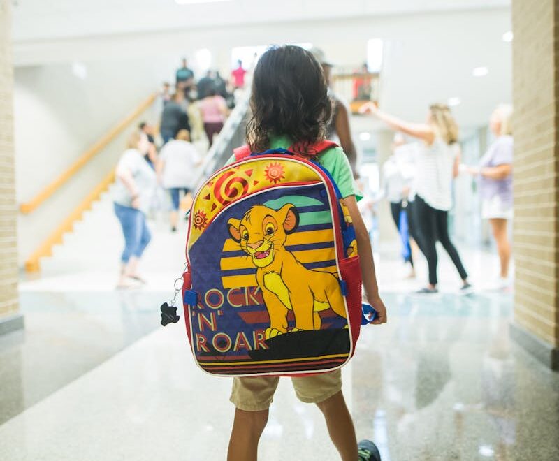 Unrecognizable child with backpack walking in crowded hall